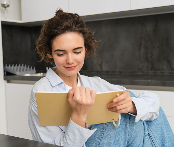 A woman reading a book while sitting on a kitchen counter
